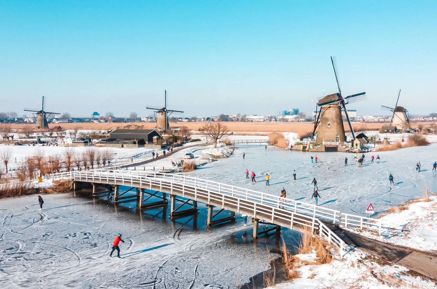 People ice skating along frozen canals at Kinderdijk with historic Dutch windmills in the background